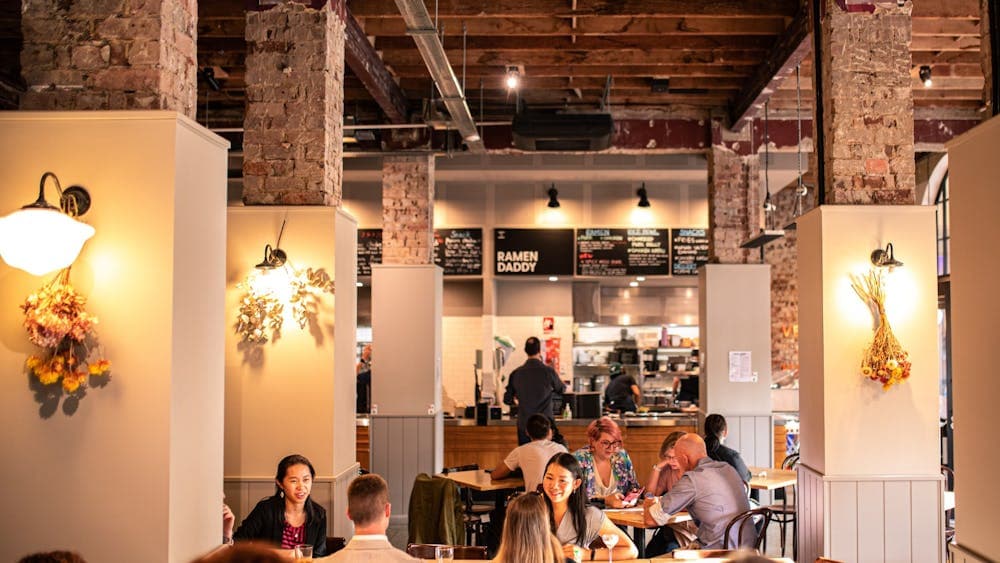 Food hall with people sitting beside columns with lights and dried flowers