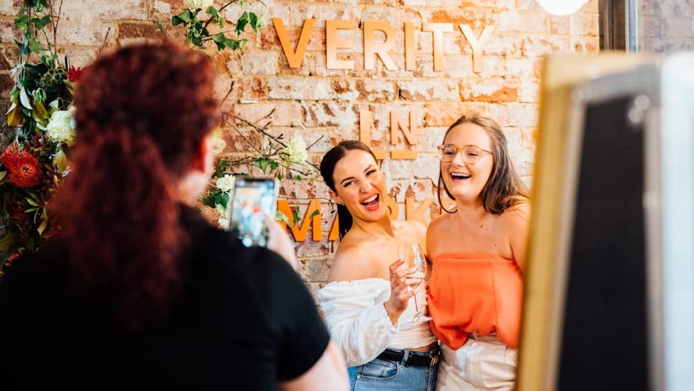 People taking photo in front of Verity Lane Market logo next to flowers