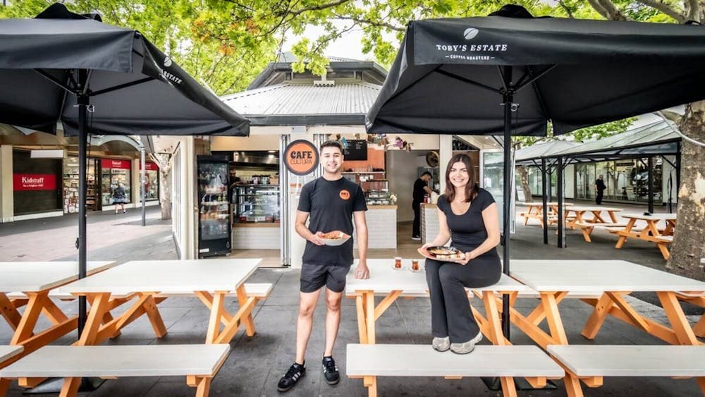 Two Cafe Cultura workers standing outside of the cafe, holding plates of food.