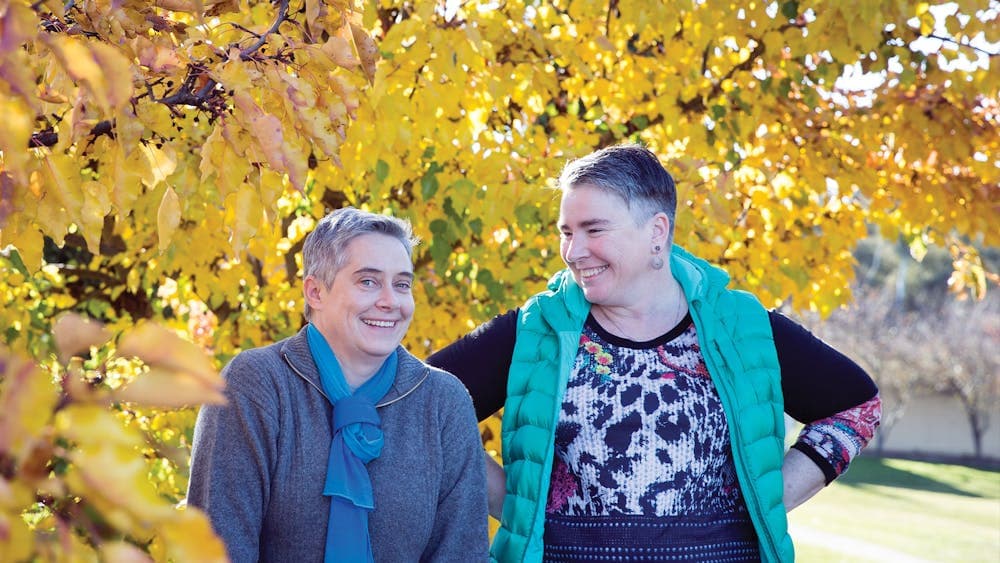 Two women standing happily under a tree with yellow leaves during Autumn in Canberra