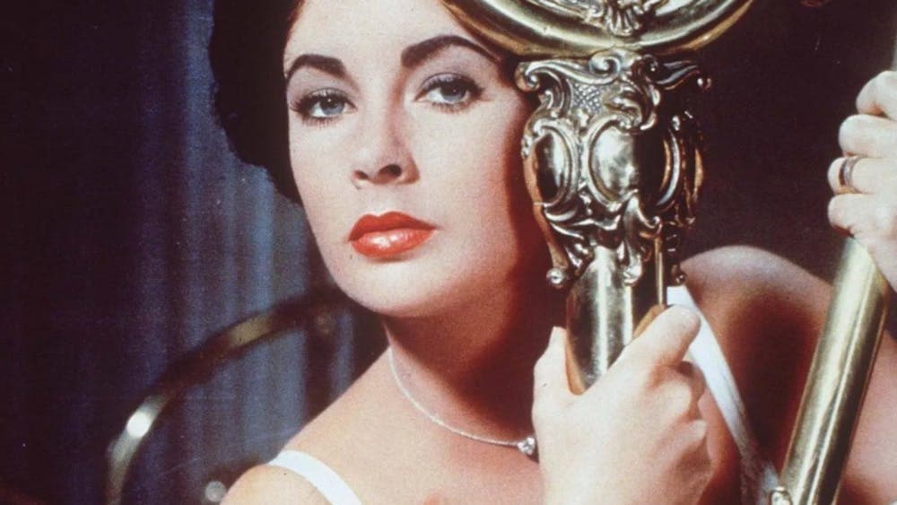 Woman holds onto gold pole looking ominously at camera