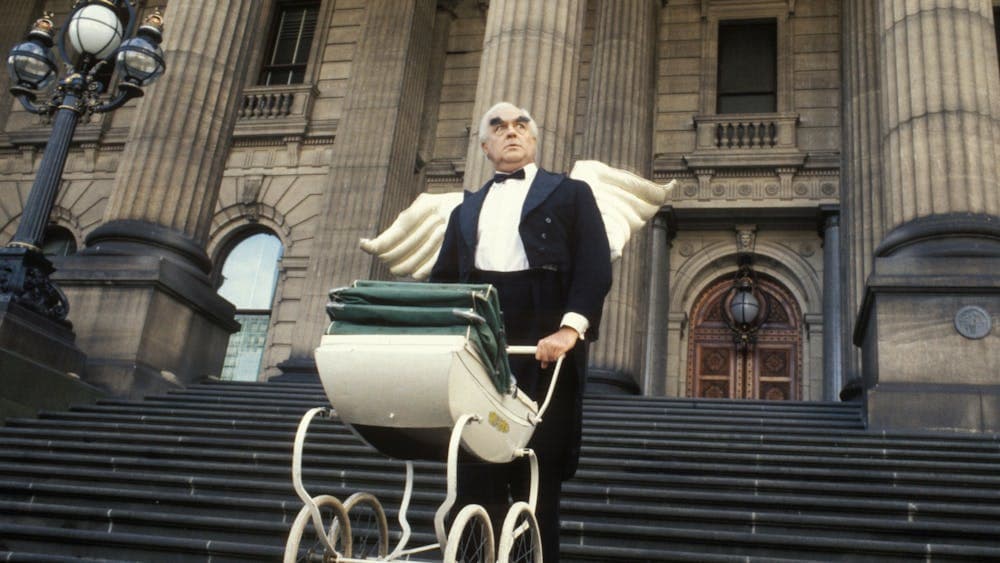 Man walking down stairs pushing a pram wearing angel wings and a suit and bowtie
