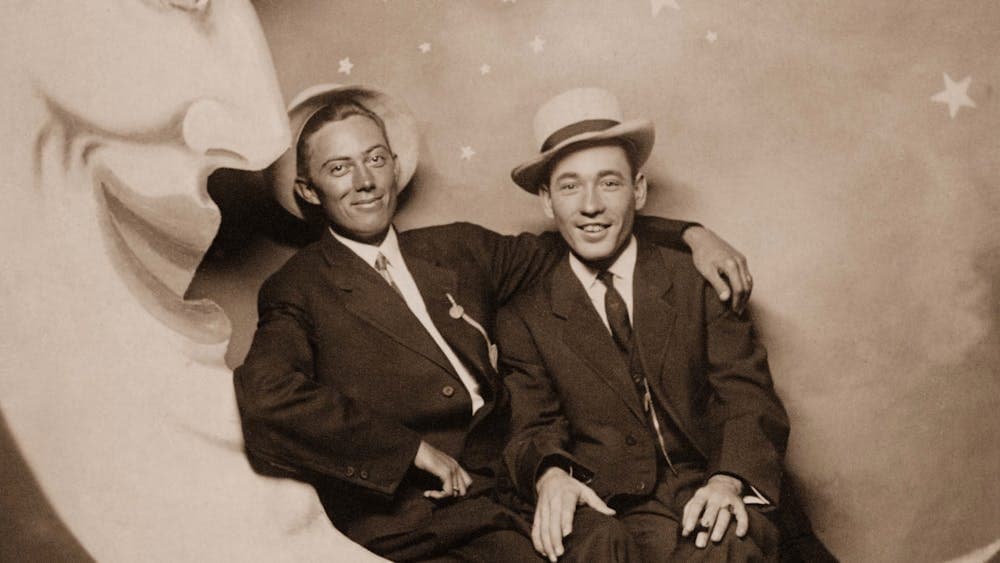Archival image of two men sitting on a sign of a crescent moon looking at camera