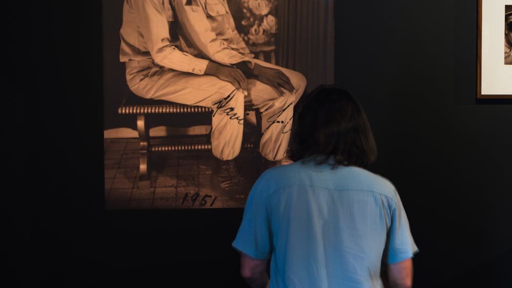 Man observes photograph of two men, one sitting on the others lap in the LOVING exhibition at CMAG