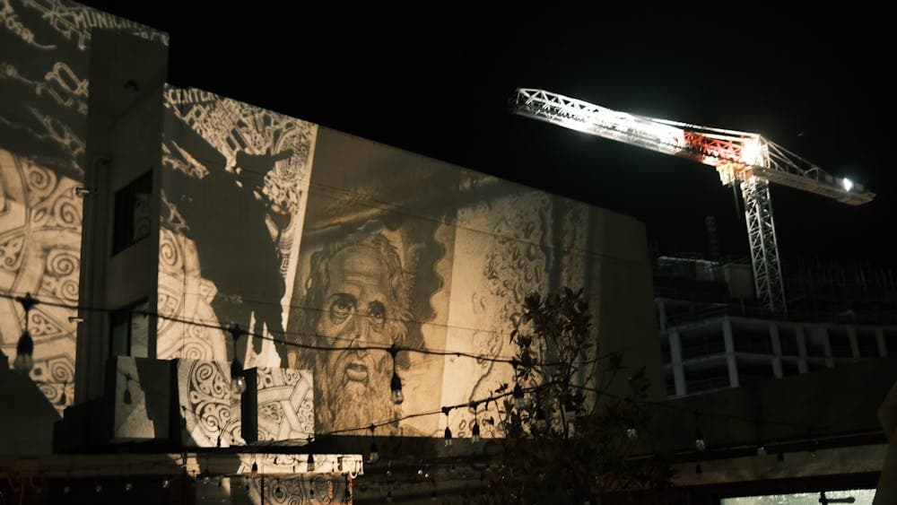 A projected artwork of a God-like figure staring at an illuminated construction crane.