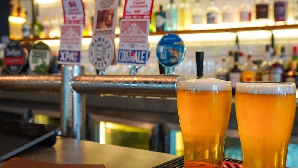 Two beers sitting on a bar in front of the bar taps