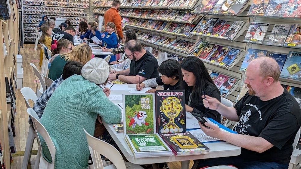 Adults and children sitting at tables in a comic shop drawing on paper