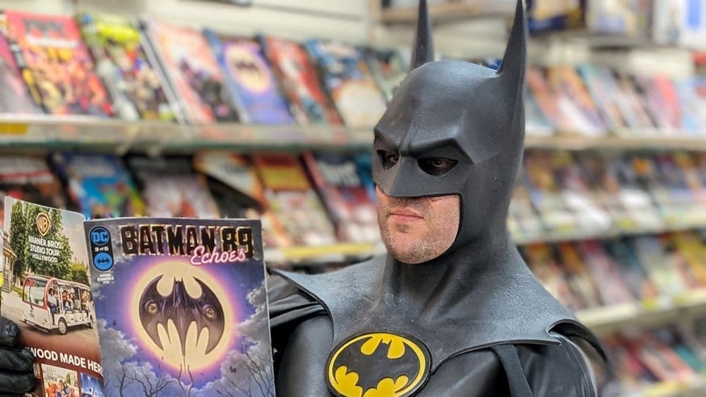 A man dressed as Batman reads a comic book inside a comic shop