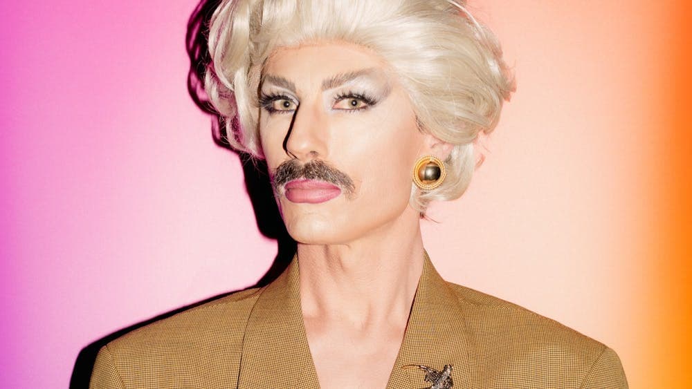 Drag artist man wearing a blonde wig and brown moustache
