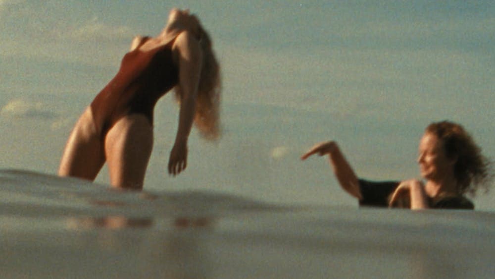 Woman in bathing suit standing in water leaning back with another woman flicking water at her