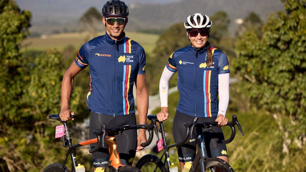 Male and female cyclist standing in scenic background smiling at the camera off-bikes