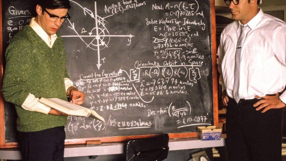 Two men stand with a blackboard with calculations on it