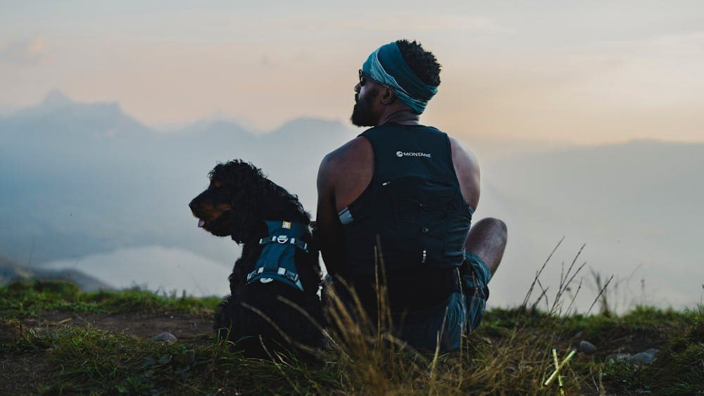 Back of man and his dog both looking left with beautiful scenery in the background