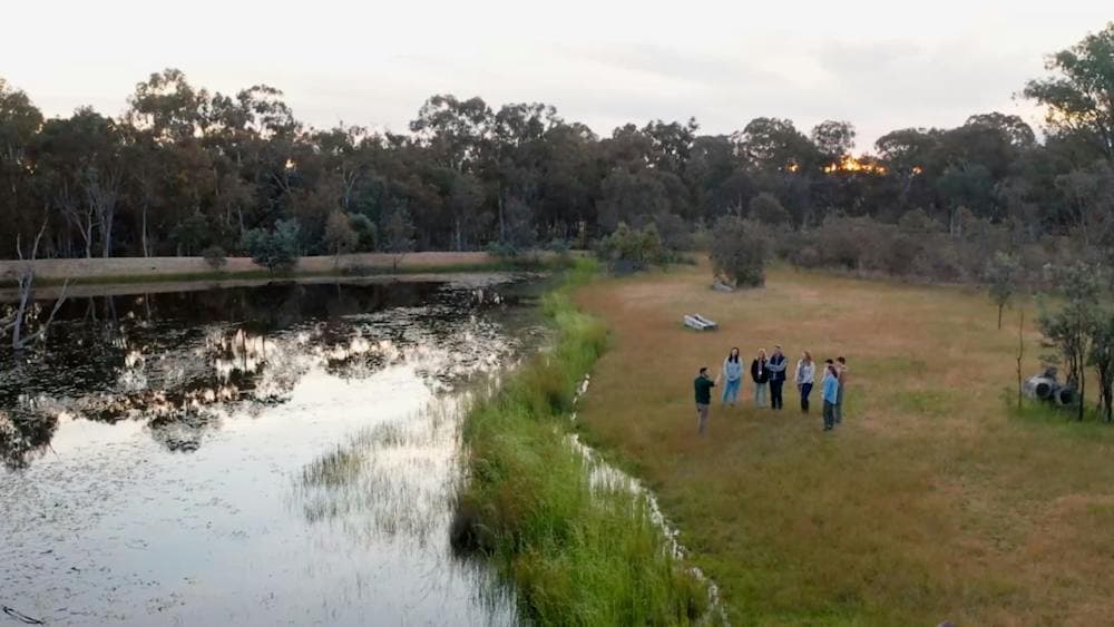 Aerial shot of guide and small group in grasslands next to dam